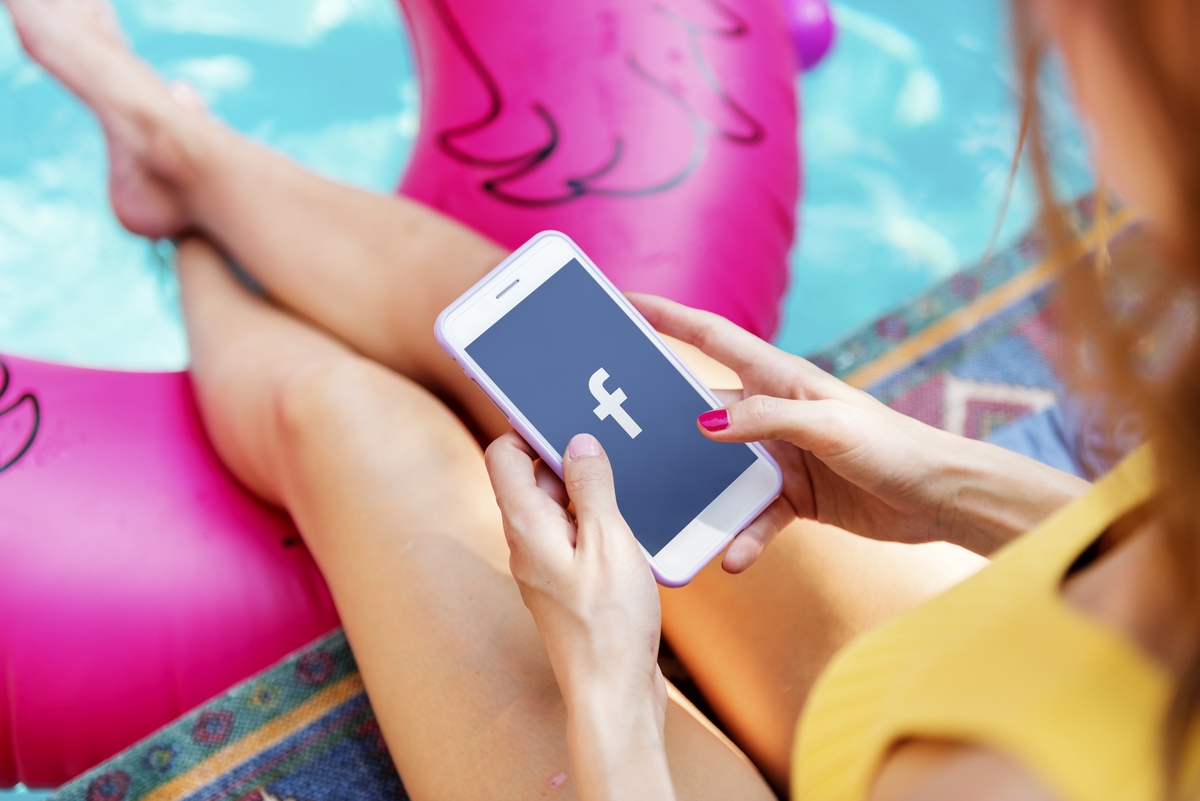 Woman using Facebook application on a phone poolside